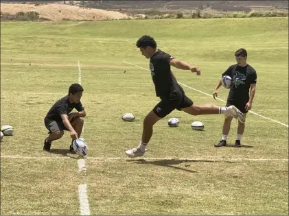  ?? The Maui News / ROBERT COLLIAS photos ?? Sione Lolohea prepares to kick a ball held by Felipe Totau as Mitchell Hirose looks on during a clinic with Baldwin High School graduate Vili Toluta‘u and a couple of his teammates from the two-time Major League Rugby champion Seattle Seawolves on Friday at Maui Lani Regional Park.