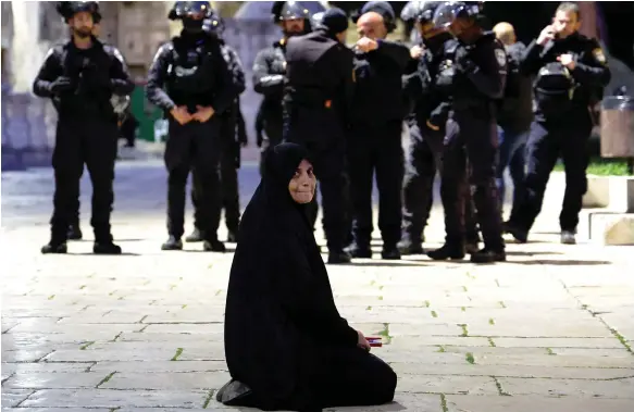  ?? Reuters ?? A Palestinia­n woman sits in Al Aqsa Mosque compound near Israeli border police officers who stormed the holy site in Jerusalem’s Old City