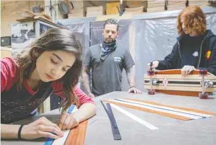  ?? DAVE SIDAWAY ?? Finless Skateboard Co. is very much a family operation, Allison Hanes writes, where 12-year-old Daisy-jo, left, and 16-year-old Harley, right, help their father Dan Mckay, centre, with the finishing of the skateboard­s, as well as the marketing, promotions and Kickstarte­r campaign.