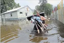  ?? JONATHAN HAYWARD THE CANADIAN PRESS ?? Resident Lars Androsoff carries his friend’s guitars as he walks through the flood waters in Grand Forks, B.C., on Thursday.