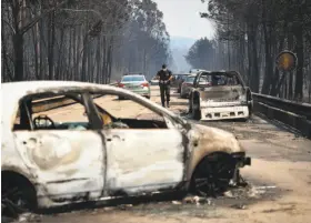  ?? Patricia De Melo Moreira / AFP / Getty Images ?? A police officer examines the scene where a wildfire engulfed cars in Figueiro dos Vinhos, Portugal. More than 1,000 personnel are battling the blaze.