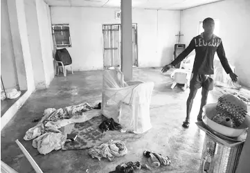  ??  ?? A man points to blood stained clothes, drums, bibles and hymn books on the bare floor, where shadowy gang dubbed the Badoo killed four worshipper­s in the Crystal Church of God at Owode Onirin in Lagos.