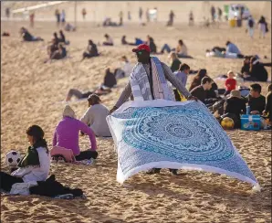  ?? (File Photo/ap/emilio Morenatti) ?? A street vendor displays sheets for sale Jan. 26 while people sunbathe on the beach in Barcelona, Spain.