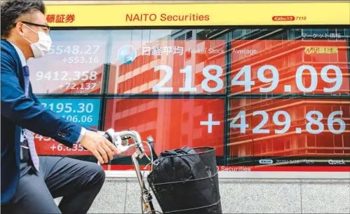  ?? (AFP) ?? A cyclist wearing a face mask rides past an electric quotation board displaying the Nikkei 225 Index in Tokyo recently.