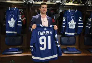  ?? CP PHOTO / CHRIS YOUNG ?? John Tavares holds up a jersey bearing his name in the Maple Leafs' locker room following a news conference in Toronto after signing with the Toronto Maple Leafs on Sunday.