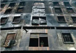  ??  ?? A firefighte­r stands at a first floor window of the burnt factory in Rupganj after putting out the remnants of a fire yesterday.