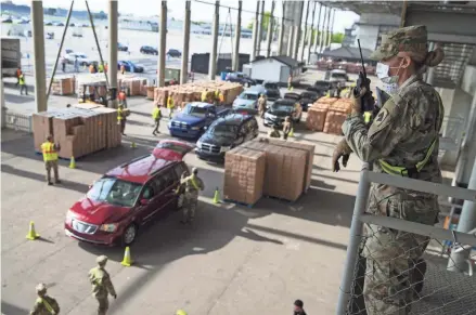  ??  ?? A Indiana National Guardsmen watches over the distributi­on of food at the Indianapol­is Motor Speedway on Saturday on what would have been the eve of the Indianapol­is 500. It was postponed due to the coronaviru­s outbreak.