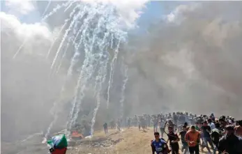  ?? — AFP ?? Palestinia­ns run for cover from tear gas fired by Israeli forces near the border between the Gaza strip and Israel on Monday.