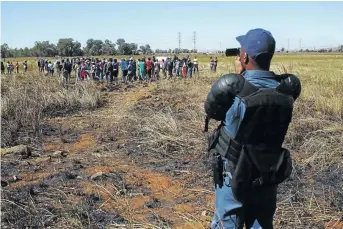  ??  ?? A police officer monitors the situation in which residents living on the outskirts of Protea Glen sought to appropriat­e vacant land for themselves .