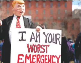  ??  ?? A PROTESTER wearing a mask depicting Trump holds a sign during a demonstrat­ion against him, on President’s Day in Washington on February 18.