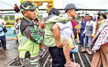  ?? — AFP photo ?? Members of an Indonesian search and rescue team assist an elderly woman (centre) as she disembarks from a ferry at the port after being evacuated from Sebesi Island, in Bakauheni in Lampung province.