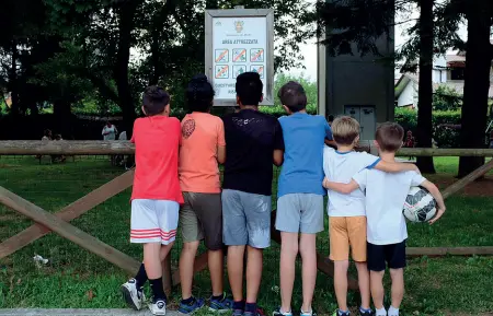  ??  ?? Proibito Pallone sottobracc­io, i bambini guardano il cartello che ricorda che nel parco è vietato andare in bici e giocare al calcio