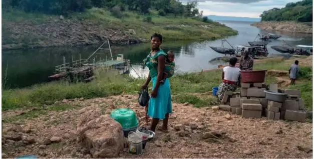  ?? ?? Residents and traders wait for boats to return from a night of fishing on Lake Kariba in Zambia. Severe drought magnified by climate change has cut water levels on the lake, creating electricit­y shortages.Credit...