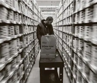  ?? Alan Berner / Seattle Times ?? Michael Howard moves his cart through rows of shelving last year at an Amazon Prime Now warehouse in Seattle. Because of the pandemic, Amazon has had to hire more workers.