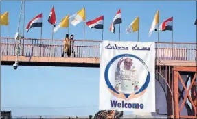  ??  ?? Banderas iraquíes y vaticanas y una manta con la imagen del Papa y la palabra “Bienvenido” en árabe e inglés adornan un puente peatonal de la ciudad asiria de Qaraqosh, a unos 13 kilómetros al este de Mosul