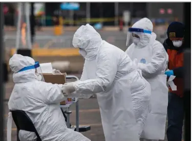  ?? (Chicago Sun-Times/Pat Nabong) ?? Medical workers help each other with their suits on Sunday at a drive-thru testing site in the parking lot of a Walmart store in
Northlake, Ill.