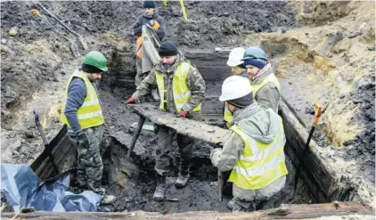  ??  ?? Archeolodz­y wynoszą drewnianą ławkę z wnętrza kilkusetle­tniej chałupy odkopanej na placu Krasińskic­h