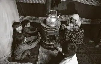  ?? Rahmat Gul / Associated Press ?? Displaced children sit around a stove to try to keep warm in a temporary shelter on Dec. 30 in Kabul, Afghanista­n.