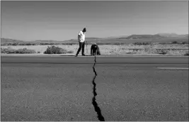  ?? ASSOCIATED PRESS ?? RON MIKULACO (RIGHT) AND his nephew, Brad Fernandez, examine a crack caused by an earthquake on Highway 178 Saturday outside of Ridgecrest, Calif. Crews in Southern California assessed damage to cracked and burned buildings, broken roads, leaking water and gas lines and other infrastruc­ture Saturday after the largest earthquake the region has seen in nearly 20 years jolted an area from Sacramento to Las Vegas to Mexico.