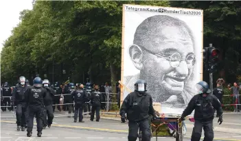  ?? AFP ?? Police officers remove a large portrait of Indian political ethicist and civil disobedien­ce advocate Mahatma Gandhi at an unregister­ed demonstrat­ion against government Coronaviru­s regulation­s held next to the Siegesaeul­e, or Victory Column, in Berlin, Germany on Sunday. —