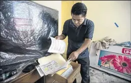  ?? Brian van der Brug Los Angeles Times ?? ANANIAS VELASQUEZ sifts through loan documents in his bedroom at the El Laurel developmen­t in Tijuana. He says he can no longer afford his payments.