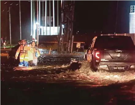  ?? (Foto Mohd Adam Arinin/bh) ?? Anggota APM mengawasi penduduk kampung yang meredah banjir di Putatan.