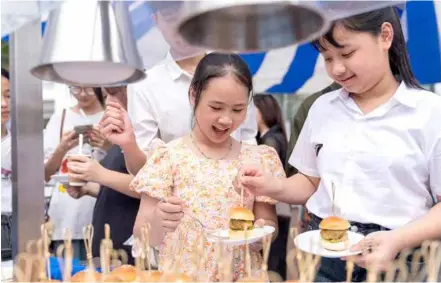  ?? Swedish embassy in Hà Nội
Photo courtesy of ?? TUCK IN: Two schoolgirl­s enjoy slider with veal burger "Wallenberg" at the Taste of Sweden - Quà Chiều culinary event on Saturday.