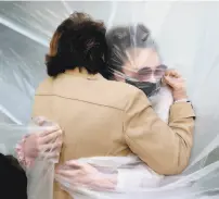  ?? Al Bello / Getty Images ?? Olivia Grant (right) hugs her grandmothe­r, Mary Grace Sileo, through a plastic drop cloth hung on a homemade clotheslin­e over Memorial Day weekend in Wantagh, N.Y.