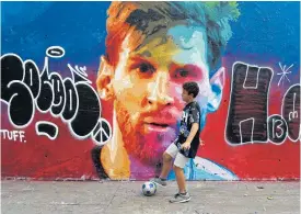  ??  ?? A boy plays football in front of a graffiti image of Lionel Messi in Barcelona.