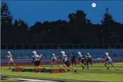  ?? RAY CHAVEZ — STAFF PHOTOGRAPH­ER ?? Members of the Palo Alto High School football team practice as the full moon rises over Palo Alto on Feb. 26.