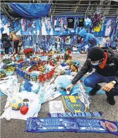  ?? ALESSANDRO GAROFALO AP ?? Fans look at the memorabili­a hanging on the gates of the San Paolo stadium in Naples, Italy, on Sunday where Diego Maradona once played.