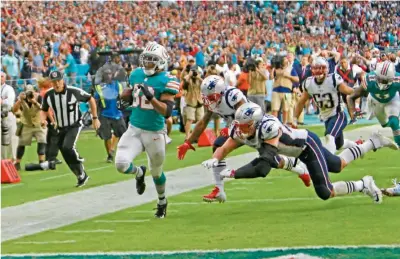  ??  ?? INALCANZAB­LE. Kenyan Drake se escapa de los jugadores de Patriots, para sellar el triunfo con el reloj en ceros, en Miami.