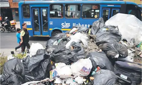  ??  ?? ► Un grupo de personas camina junto una columna de basura en Bogotá, el lunes.