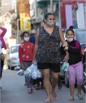  ?? AP ?? Residentes de Paraisópol­is, en São Paulo, regresan a casa después de recibir kits con productos de limpieza.