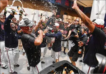  ?? BRANT SANDERLIN / BSANDERLIN@AJC.COM ?? Manager Brian Snitker (left) leads the celebratio­n in the clubhouse after the Braves clinched the NL East by winning their third straight against the Phillies at SunTrust Park on Saturday.