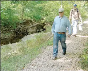  ?? Keith Bryant/The Weekly Vista ?? Tanyard Creek volunteer Randy Hamm, left, foreground, walks into the Tanyard Creek Nature Trail, tools in hand, while fellow volunteer Dave Murphy follows with buckets of supplies.