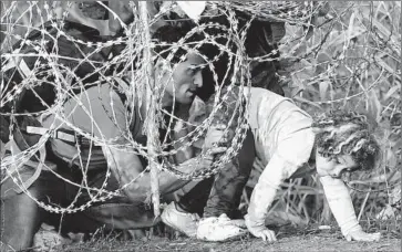  ?? Attila Kisbenedek AFP/Getty Images ?? A GIRL gets help from her father as they breach a fence near the border village of Roszke in Hungary. Many migrants who cross the Mediterran­ean use Serbia and Hungary as a gateway to wealthier European nations.