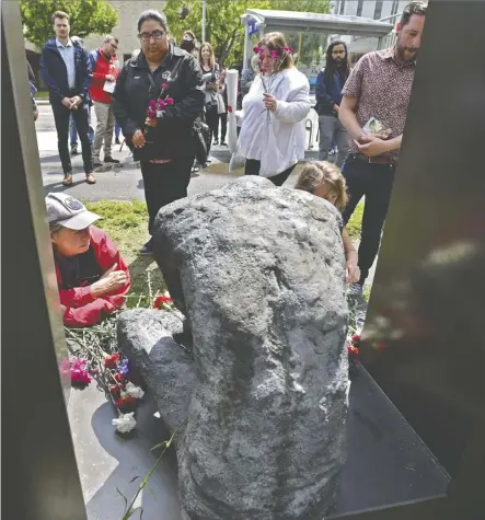  ?? Ed Kaiser ?? People lay commemorat­ive flowers Tuesday at the Homeless Memorial Plaza across from city hall during the 14th annual service to honour people who died in situations of homelessne­ss or poor housing.