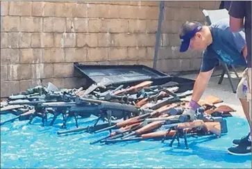  ?? Linnard Lane
Palisadian Post ?? A MAN inspects weapons found during a death investigat­ion in Pacific Palisades. About 1,500 firearms — along with 6.5 tons of ammunition, which probably will be destroyed — were found in Jeffrey Alan Lash’s home.