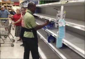  ?? WILFREDO LEE — THE ASSOCIATED PRESS ?? An employee restocks bottled water on bare shelves as customers look on at a Publix grocery store, Tuesday in Surfside, Fla.