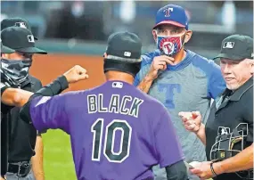  ??  ?? Sign of the times during the coronaviru­s pandemic: Rangers manager Chris Woodward adjusts his face mask while Rockies manager Bud Black exchanges elbow bumps with an umpire before an exhibition game Tuesday in Arlington, Texas.