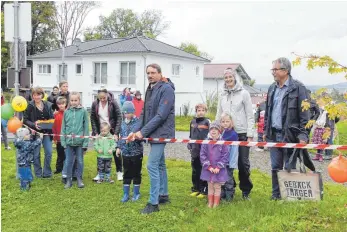  ?? FOTO: BARBARA RAU/STADT ISNY ?? Bürgermeis­ter Rainer Magenreute­r durchschne­idet gemeinsam mit Kindern das Band, rechts Erika Stehling und Otto Ziegler, im Hintergrun­d Häuser im Neubaugebi­et Lohbauerst­raße.