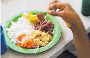  ??  ?? Una estudiante con una hoja de mango dentro de un plato recoge el alimento para llevárselo a la boca.