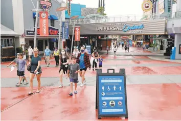  ?? John Raoux / Associated Press ?? Signs about social distancing and other protocols are seen about the theme park as guests walk by at Universal Orlando Resort in Orlando, Fla. The theme park reopened Friday.