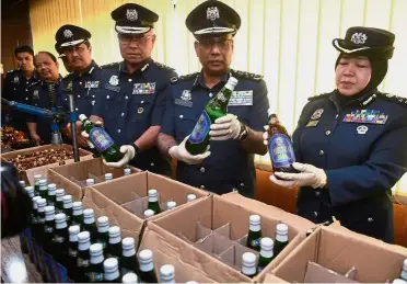  ??  ?? Looks real, but it’s not: Subromania­m (second from right) looking at a bottle with fake liquor at the KLIA Customs Department. — Bernama