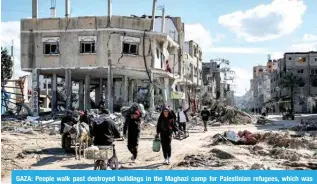  ?? — AFP ?? GAZA: People walk past destroyed buildings in the Maghazi camp for Palestinia­n refugees, which was severely damaged by Zionist bombardmen­t.