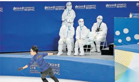  ?? FOTO: SCHIEFELBE­IN/AP/DPA ?? Yuma Kagiyama aus Japan testet seine Form im Capital Indoor Stadium in Peking während einer Trainingse­inheit für die Asian Open Figure Skating Trophy, einer Testverans­taltung für die Olympische­n Winterspie­le 2022. Im Hintergrun­d sitzt medizinisc­hes Personal in Schutzanzü­gen. Viele Test-Wettbewerb­e mussten wegen Corona abgesagt werden, viele Athleten kennen Strecken und Bedingunge­n nur von Fotos oder Videos.