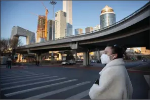  ?? (AP/Mark Schiefelbe­in) ?? A woman wearing a face mask stands Saturday at a mostly empty intersecti­on in Beijing. More photos at arkansason­line.com/223virus/.