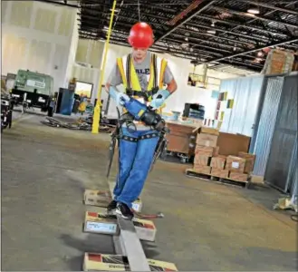  ??  ?? Henderson High School senior Owen Downing tries his hand at walking across a steel beam while wearing personal safety gear and carrying ironworker tools.