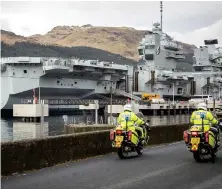  ??  ?? Police officers ride past the Royal Navy aircraft carrier HMS Queen Elizabeth at Glen Mallan, in Loch Long, as the vessel visits western Scotland